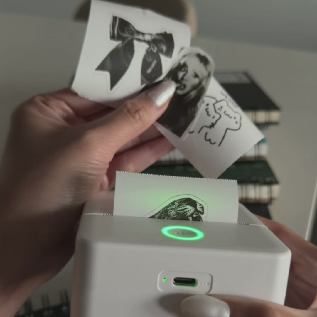 Load video: A woman using the Corixa Pocket Sticker Printer to print custom stickers for her journal.